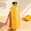 clear-pet-square-juice-bottle-filled-with-orange-juice-and-held-in-hand.jpg